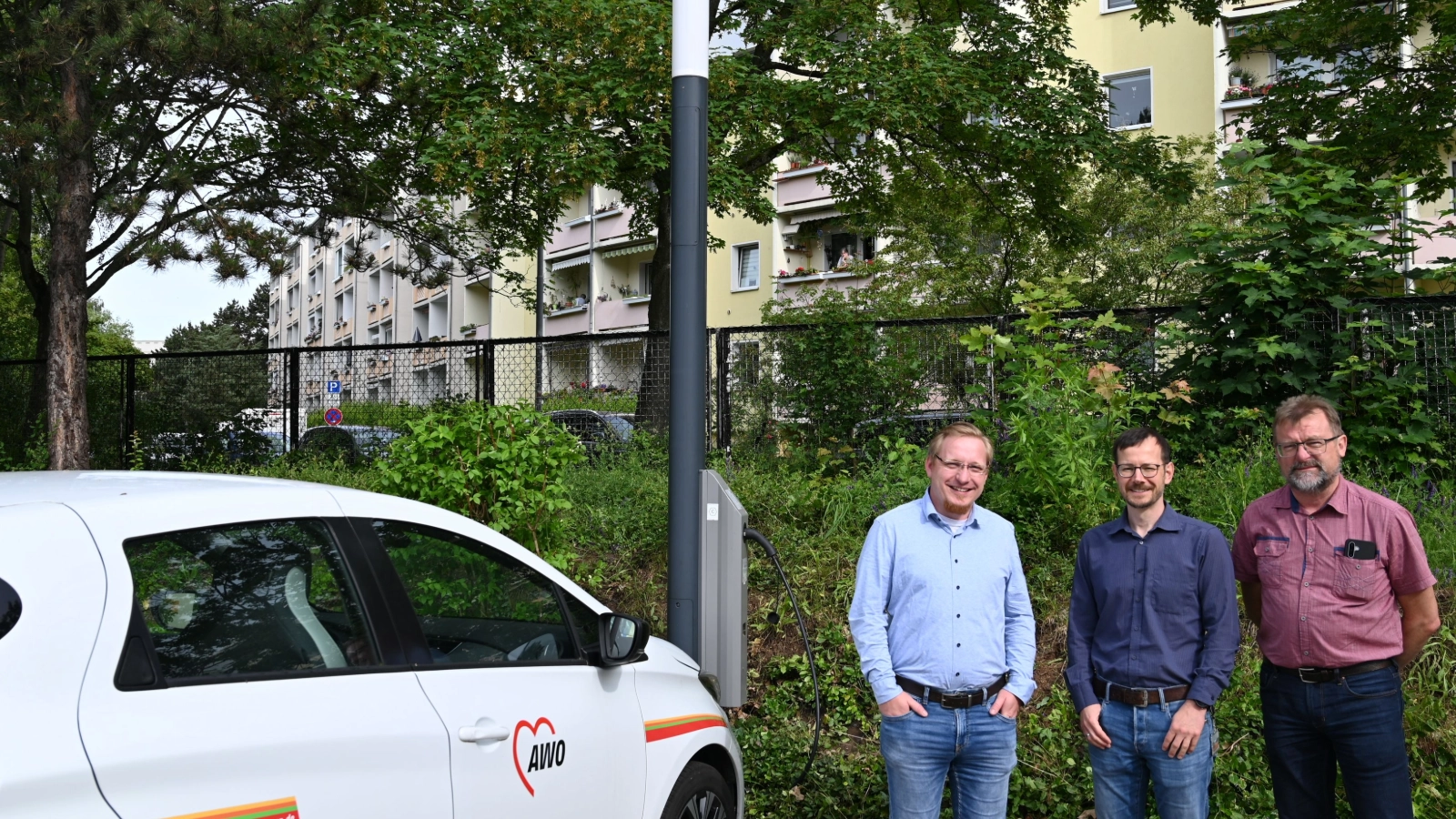 Frank Burkert, Leiter der Tagespflege im AWO Wohnpark Lebenszeit, Andreas Well von den Stadtwerken Energie Jena-Pößneck und Heiko Hirte, Projektmitarbeiter im Projekt JenErgieReal neben dem neuen Laternenlader auf dem Parkplatz der Tagespflege in der Rudolf-Breitscheid-Straße in Jena-Lobeda. 