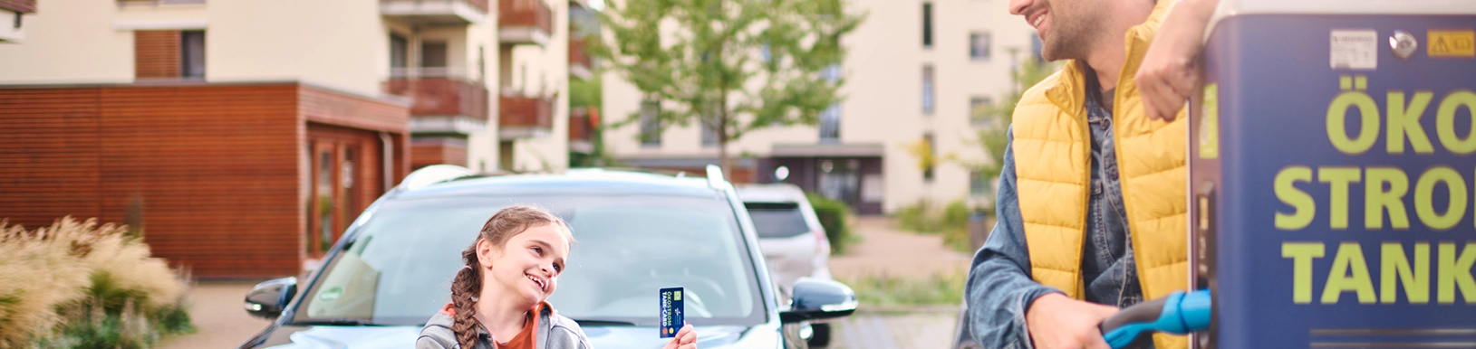 Ein Vater steht mit seiner Tochter an einer E-Ladestation