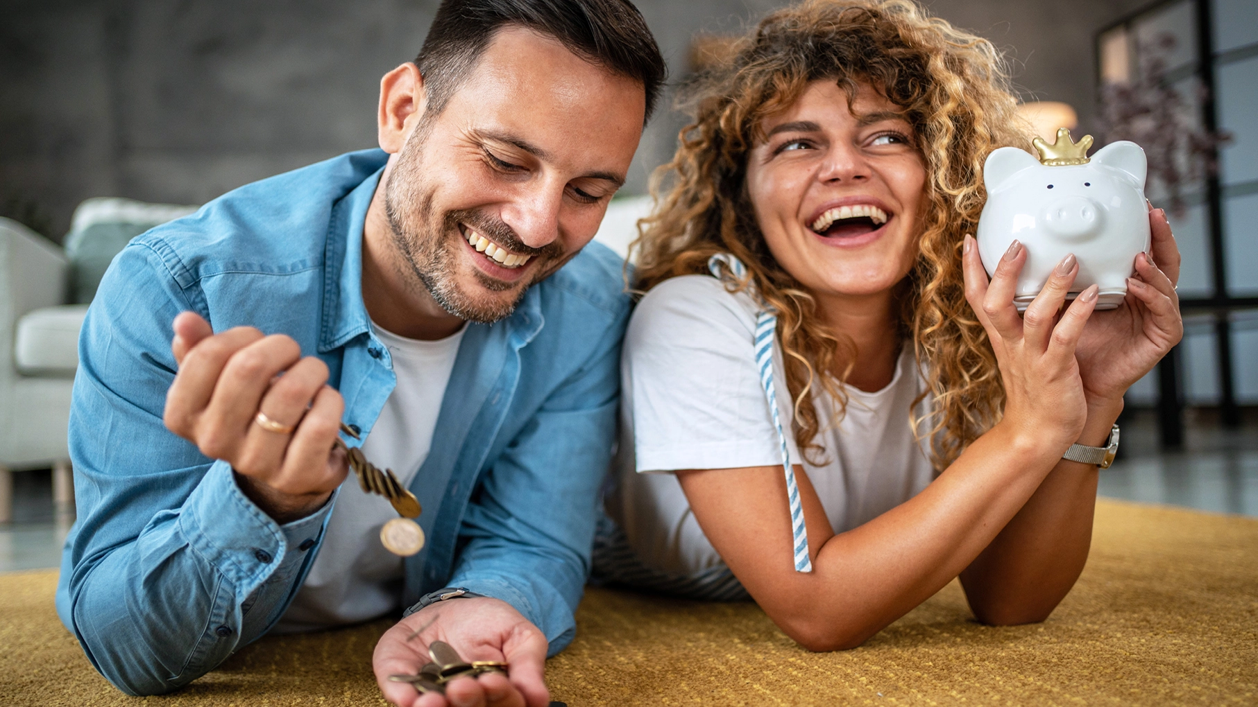 Junger Mann und junge Frau, lachend, mit Sparschwein und Geldmünzen