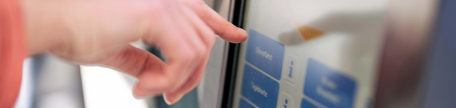 Eine Hand tippt auf das Display eines Fahrscheinautomaten im Fahrzeug.