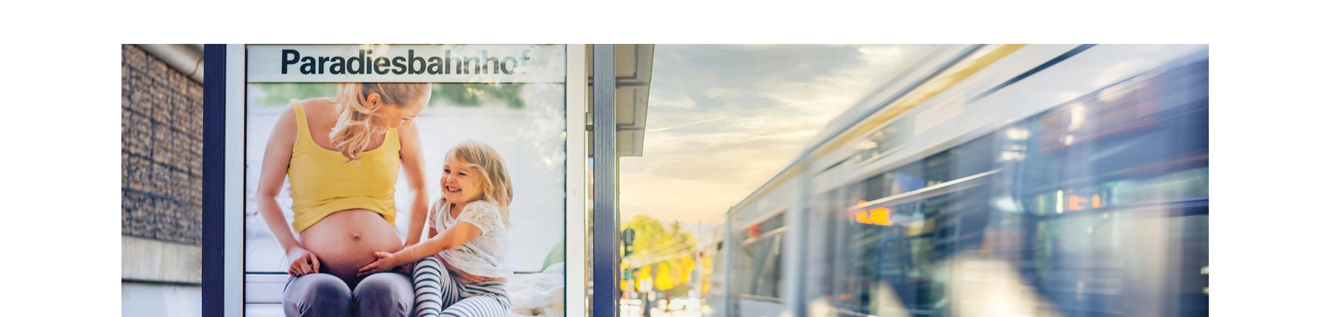 Eine Haltestelle mit Werbung der AOK. Eine Straßenbahn fährt an der Haltestelle vorbei.