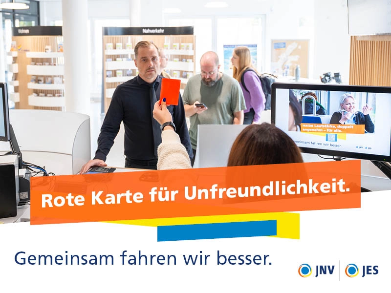 Eine Mitarbeiterin zeigt einem Kunden am Schalter die rote Karte.